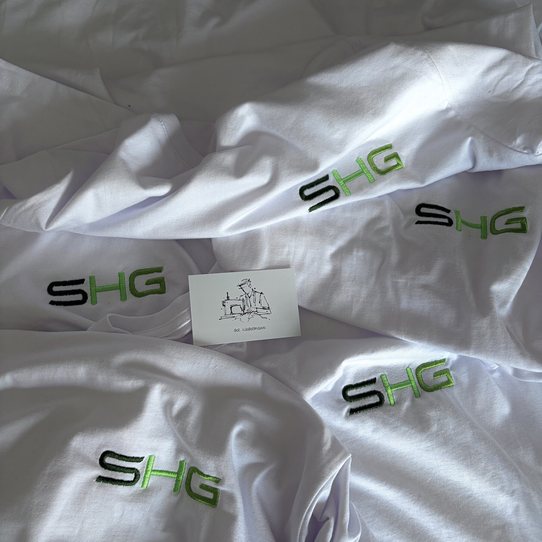 Weiße Shirts mit gesticktem SHG Gartenbau Logo in Schwarz und Grün