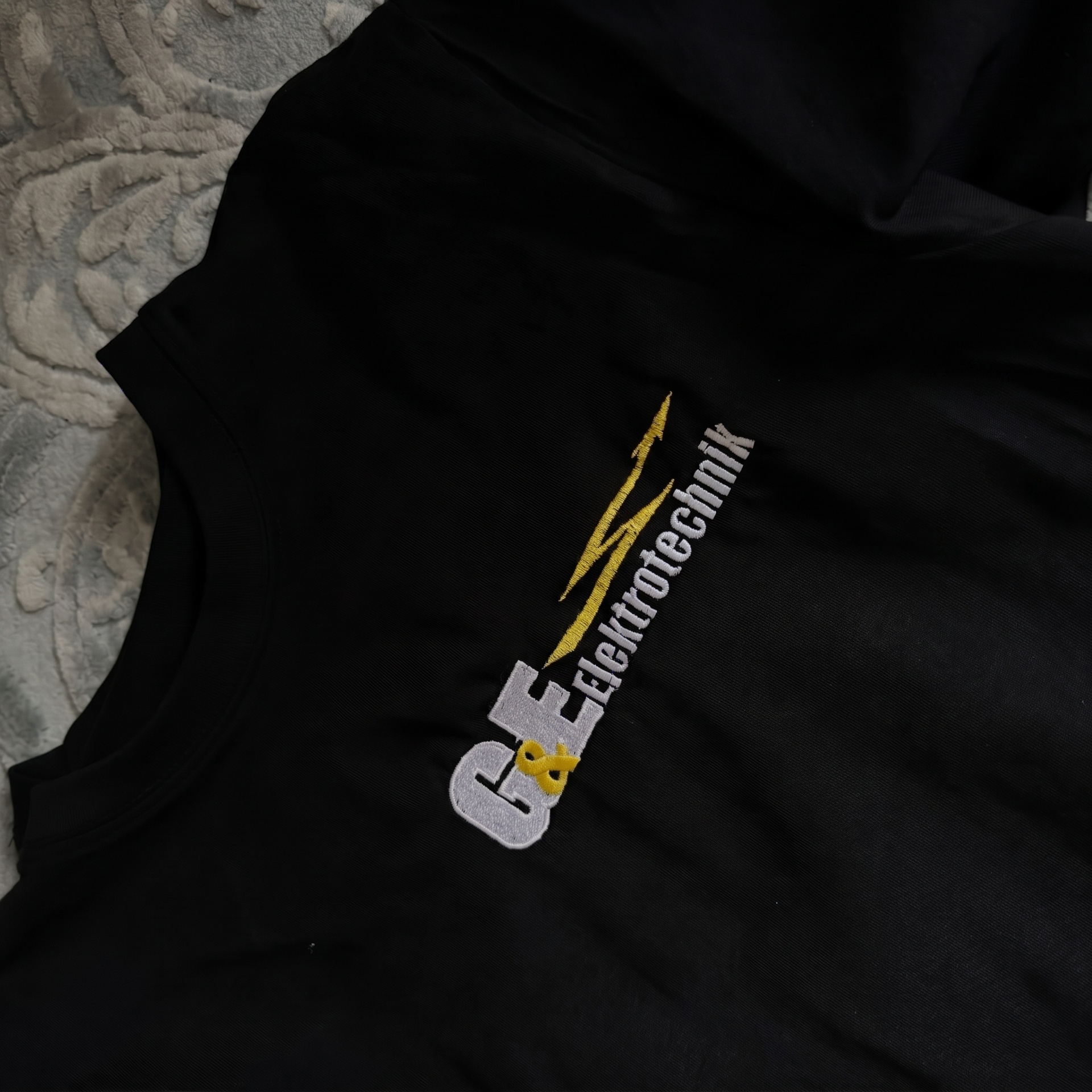 Schwarzes Shirt mit gestickter G&E Elektrotechnik Logo-Stickerei mit gelbem Blitz